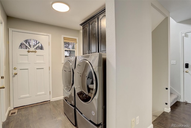 clothes washing area with dark wood-style flooring, visible vents, baseboards, washer and dryer, and cabinet space