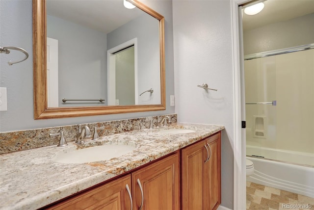 full bathroom featuring toilet, double vanity, combined bath / shower with glass door, and a sink