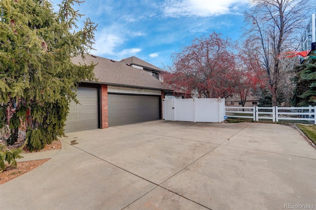 view of home's exterior with brick siding, a shingled roof, concrete driveway, an attached garage, and fence