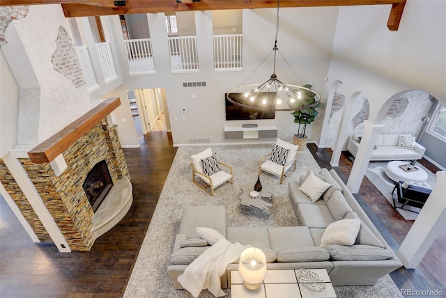 living area featuring dark wood finished floors, visible vents, a high ceiling, a stone fireplace, and baseboards