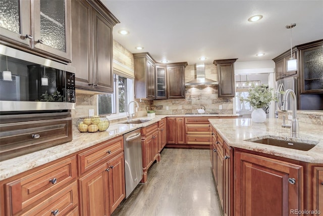 kitchen with decorative light fixtures, stainless steel appliances, a sink, wall chimney range hood, and glass insert cabinets