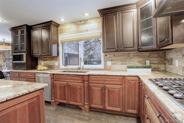 kitchen with wall chimney range hood, appliances with stainless steel finishes, a sink, and glass insert cabinets