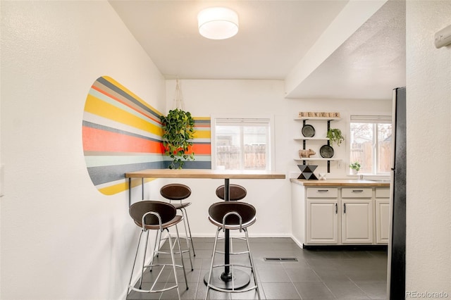 kitchen featuring visible vents, freestanding refrigerator, white cabinets, dark tile patterned floors, and baseboards