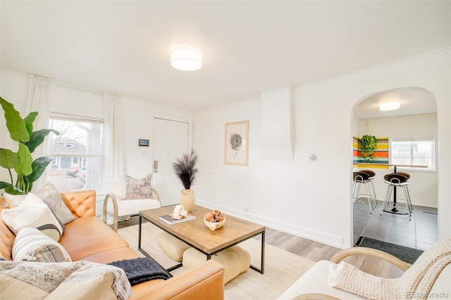 living area featuring light wood-style floors, arched walkways, and baseboards