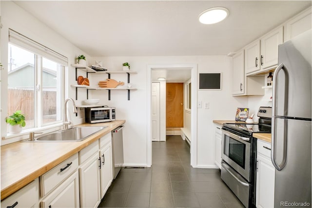 kitchen featuring open shelves, white cabinetry, stainless steel appliances, and a sink