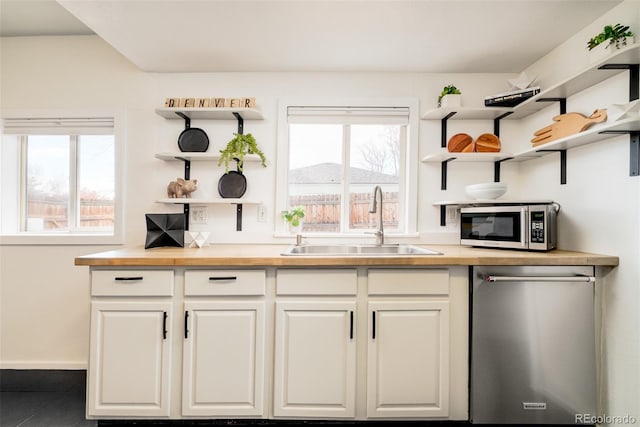 kitchen with open shelves, stainless steel appliances, a sink, wood counters, and plenty of natural light