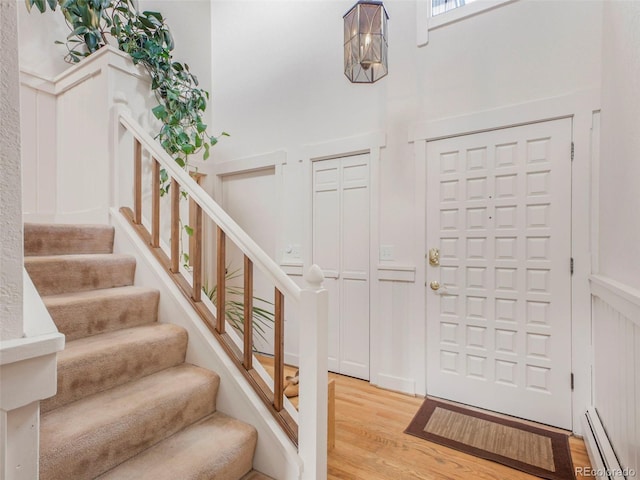 foyer entrance featuring stairway, light wood-type flooring, and a baseboard heating unit