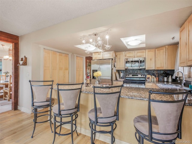 kitchen featuring an inviting chandelier, light brown cabinetry, a sink, light wood-type flooring, and appliances with stainless steel finishes
