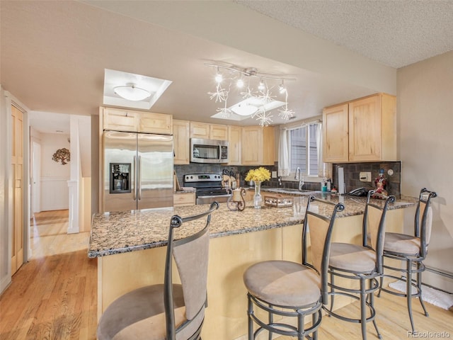 kitchen featuring stainless steel appliances, light brown cabinets, light stone countertops, light wood-style floors, and tasteful backsplash