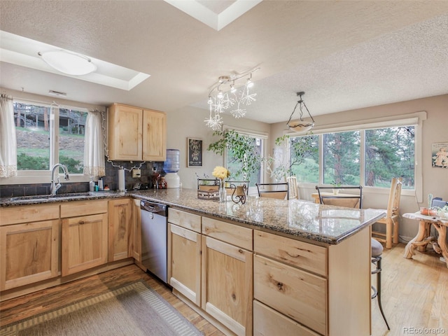 kitchen with a peninsula, light wood finished floors, light brown cabinetry, a sink, and stainless steel dishwasher