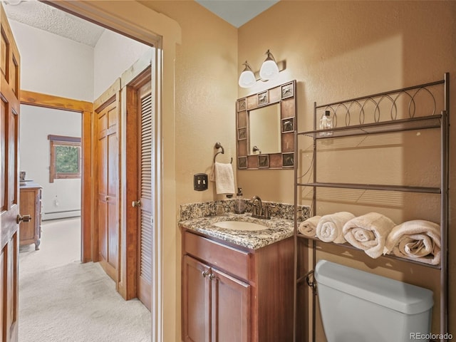 bathroom featuring toilet, baseboard heating, vanity, and a textured wall