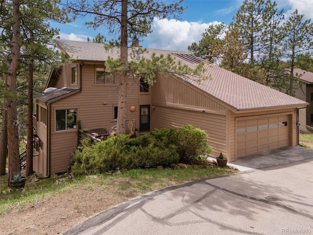 view of front of home featuring an attached garage, a chimney, and aphalt driveway