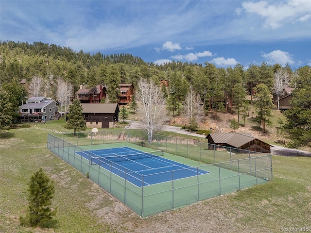 view of tennis court with a yard and fence