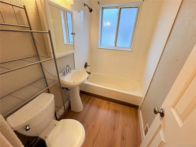 bathroom with hardwood / wood-style floors, toilet, and tiled shower / bath