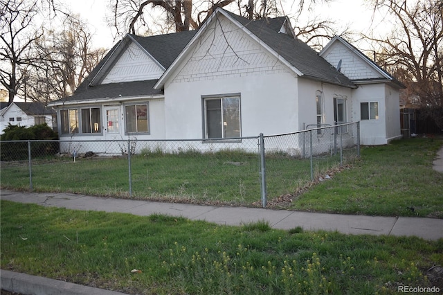 view of front facade with a shingled roof, stucco siding, a front lawn, and a fenced front yard