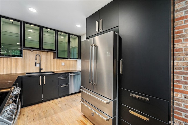 1111 Monroe St, Denver, CO 80206 - kitchen featuring stainless steel appliances, a sink, light wood-style flooring, dark cabinets, and dark countertops
