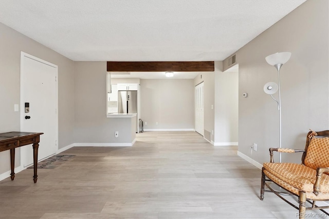 interior space with beam ceiling, light hardwood / wood-style floors, and a textured ceiling