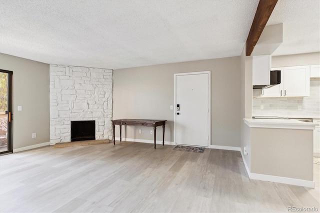 unfurnished living room featuring beam ceiling, a stone fireplace, light hardwood / wood-style floors, and a textured ceiling