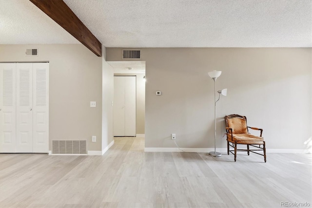 unfurnished room featuring a textured ceiling, light hardwood / wood-style flooring, and beamed ceiling