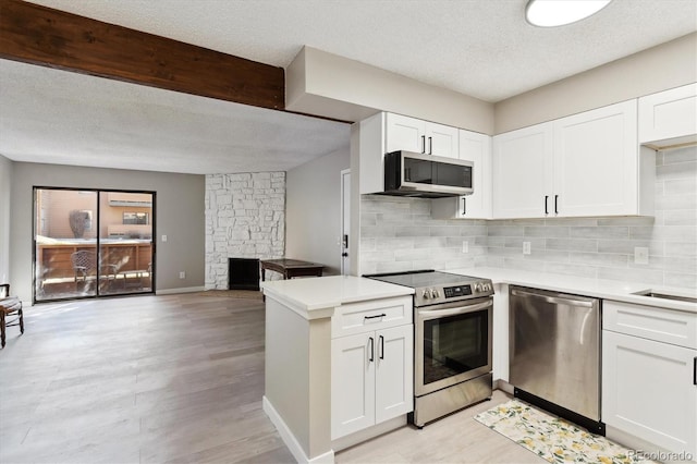 kitchen featuring a stone fireplace, stainless steel appliances, white cabinets, a textured ceiling, and decorative backsplash