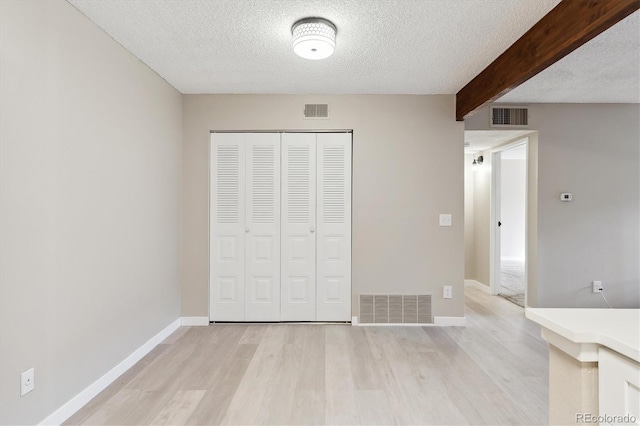 unfurnished bedroom featuring a closet, a textured ceiling, beam ceiling, and light hardwood / wood-style floors