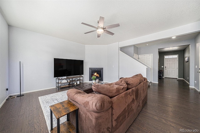 living area with a textured ceiling, dark wood-style flooring, a ceiling fan, baseboards, and a glass covered fireplace