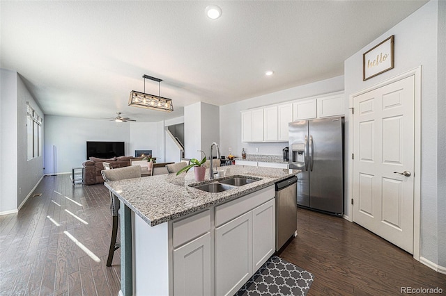 kitchen with a center island with sink, dark wood-style floors, stainless steel appliances, white cabinetry, and a sink