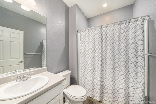 bathroom featuring toilet, a textured wall, curtained shower, and vanity