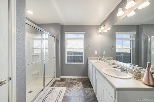 full bath with a sink, a shower stall, baseboards, and double vanity