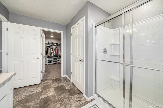 bathroom featuring a stall shower, baseboards, a walk in closet, a textured ceiling, and vanity