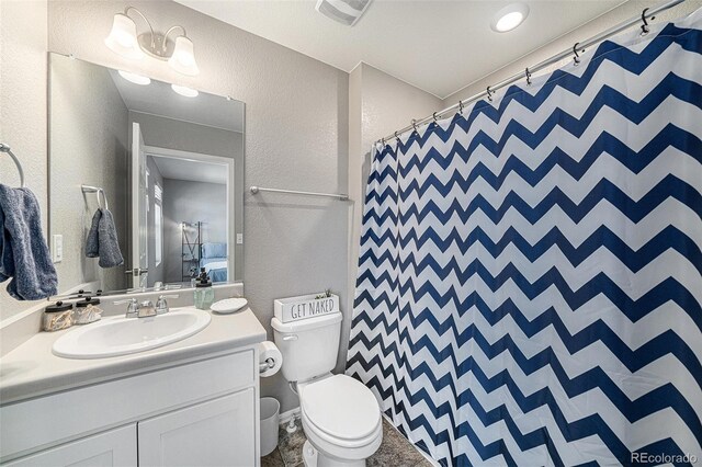 bathroom featuring visible vents, a textured wall, vanity, and toilet