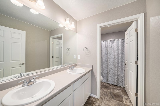 full bath with toilet, double vanity, and a sink