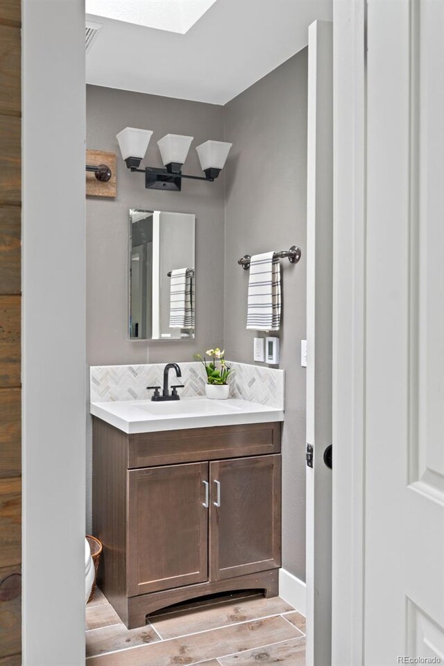 8764 W 95th Ave, Broomfield, CO 80021 - bathroom with vanity, toilet, a skylight, backsplash, and wood finished floors