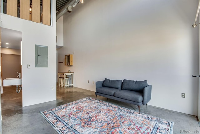 living room with electric panel, a towering ceiling, and finished concrete flooring