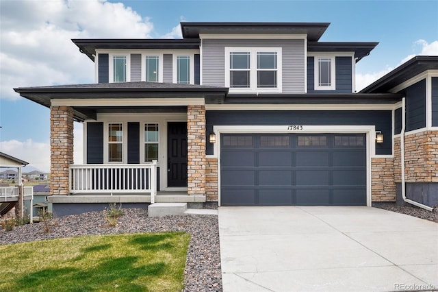 prairie-style house featuring a garage, covered porch, stone siding, and concrete driveway