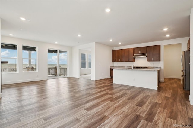 kitchen featuring freestanding refrigerator, recessed lighting, open floor plan, wood finished floors, and under cabinet range hood