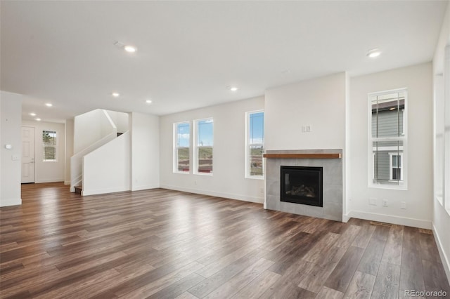 unfurnished living room featuring a tiled fireplace, baseboards, recessed lighting, and wood finished floors