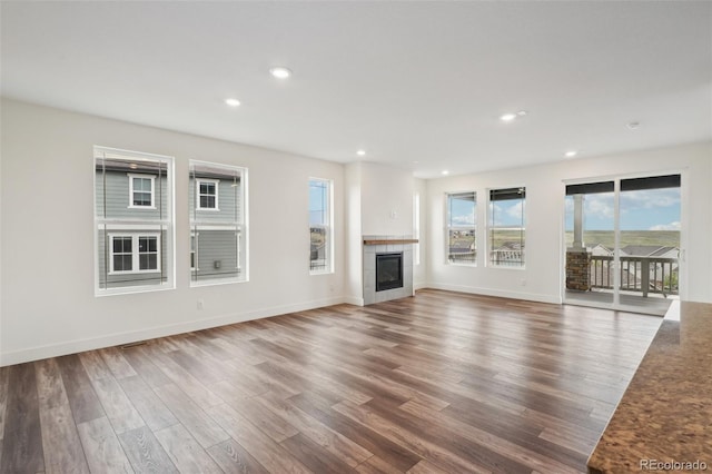 unfurnished living room with recessed lighting, wood finished floors, a wealth of natural light, and a tile fireplace