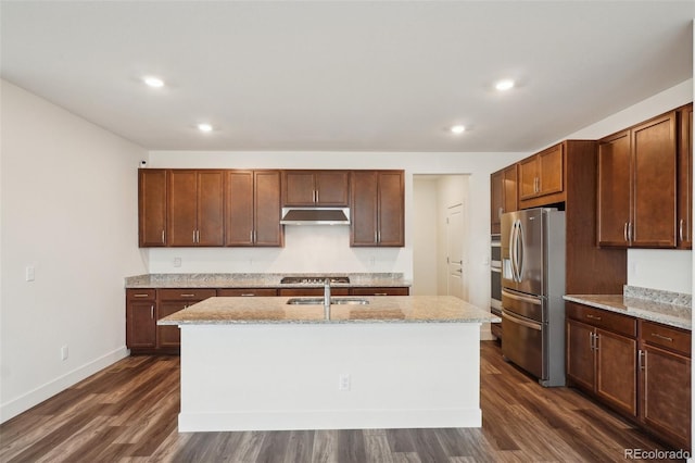 kitchen featuring dark wood-type flooring, under cabinet range hood, stainless steel appliances, recessed lighting, and an island with sink