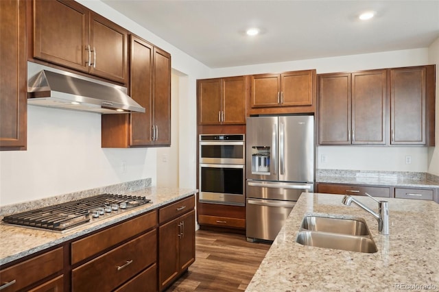kitchen with under cabinet range hood, light stone counters, a sink, dark wood finished floors, and appliances with stainless steel finishes
