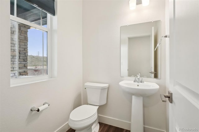 half bath with toilet, baseboards, a sink, and wood finished floors