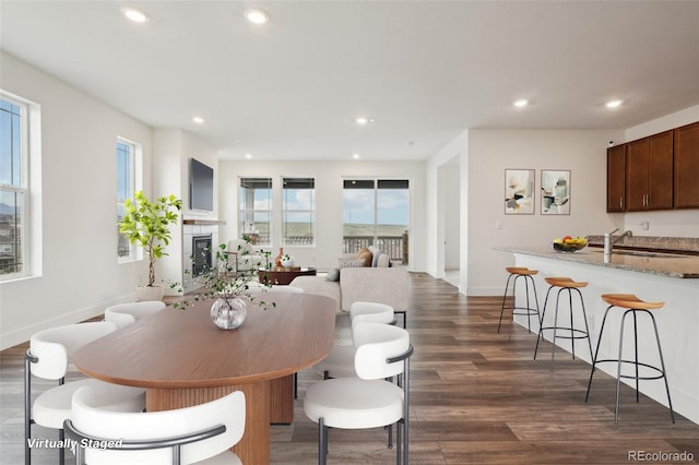 dining room featuring dark wood-style flooring, recessed lighting, baseboards, and a glass covered fireplace