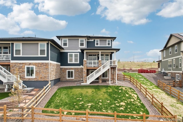 back of property featuring stairs, a fenced backyard, a lawn, and stone siding