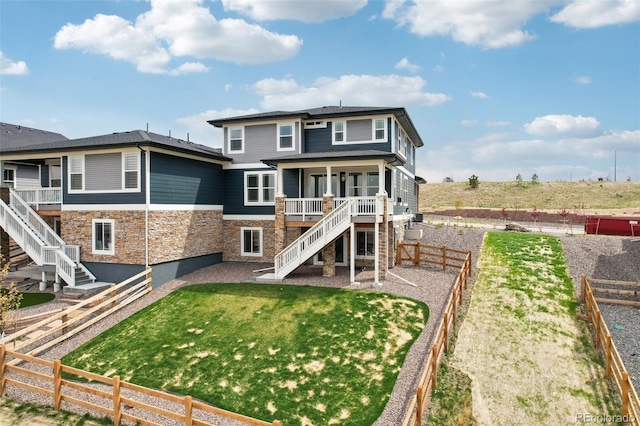 rear view of house featuring a yard, a fenced backyard, stairs, and stone siding