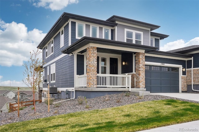 prairie-style home featuring a porch, driveway, a garage, central air condition unit, and stone siding