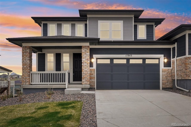 prairie-style home with a porch, driveway, stone siding, and a garage