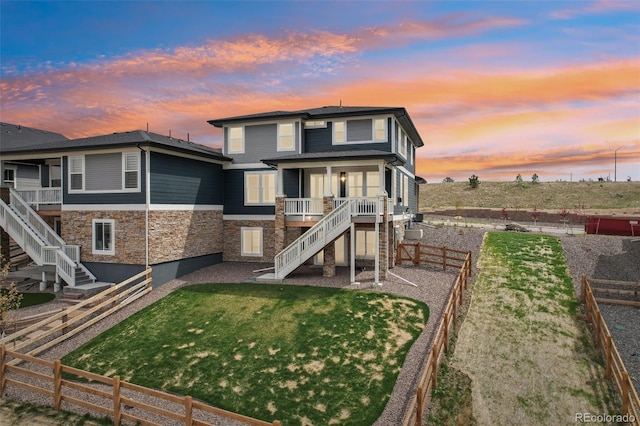 back of property at dusk featuring a lawn, a fenced backyard, stone siding, and stairway