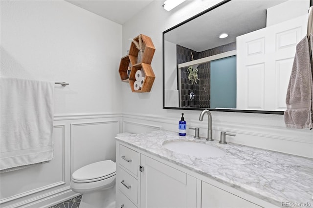 bathroom featuring a wainscoted wall, a decorative wall, toilet, a shower with shower door, and vanity