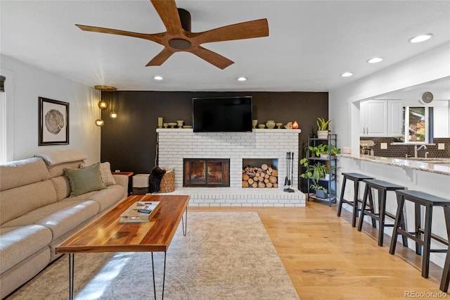 living room featuring ceiling fan, a brick fireplace, sink, and light wood-type flooring