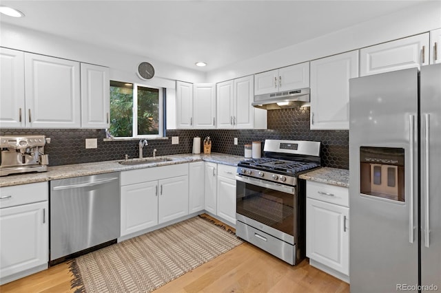 kitchen featuring appliances with stainless steel finishes, light wood-style floors, white cabinets, a sink, and under cabinet range hood